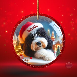 K&ouml;nnte beinhalten: Weihnachtsschmuck mit einem schwarz-wei&szlig;en Hund mit Weihnachtsm&uuml;tze und dem Namen "Bernie". Der Schmuck befindet sich in einer durchsichtigen Glaskugel mit rotem Glitzerrahmen, vor rotem Hintergrund mit festlichen Elementen.