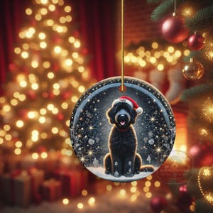 May include: Round Christmas ornament featuring a black dog wearing a Santa hat, set against a snowy winter scene with twinkling lights. The ornament is suspended by a gold string, with a Christmas tree and festive decorations in the background.