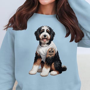 A woman wearing a light blue sweatshirt with a graphic of a dog, specifically a Bernese Mountain Dog, on the front.