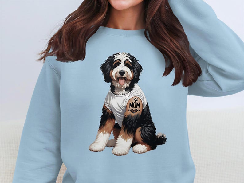 A woman wearing a light blue sweatshirt with a graphic of a dog, specifically a Bernese Mountain Dog, on the front.