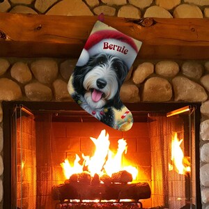 Op de afbeelding: Een kerstsok met een zwart-witte hond met een kerstmuts met de naam "Bernie" erop. De sok hangt boven een open haard met een brandend vuur.