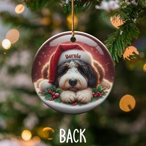 Personalize your holiday decor with this charming Bernedoodle Christmas ornament! Featuring a cute Bernedoodle in a festive Santa hat and customizable name, this round ornament adds warmth and joy to any tree. Perfect for dog lovers and unique gifts!