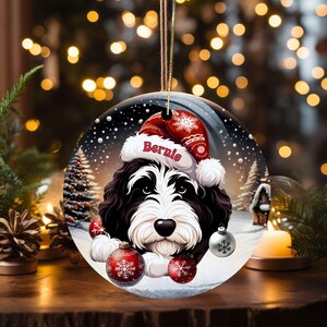 Personalize your holiday decor with this charming Bernedoodle Christmas ornament! Featuring a cute Bernedoodle in a festive Santa hat and customizable name, this round ornament adds warmth and joy to any tree. Perfect for dog lovers and unique gifts!