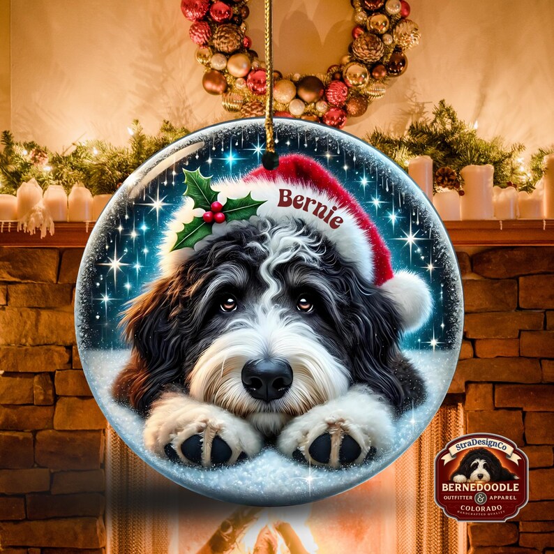 May include: A round Christmas ornament featuring a Bernedoodle dog wearing a Santa hat with the name "Bernie". The ornament has a snowy background with sparkling stars and holly. The ornament is hanging from a gold string.