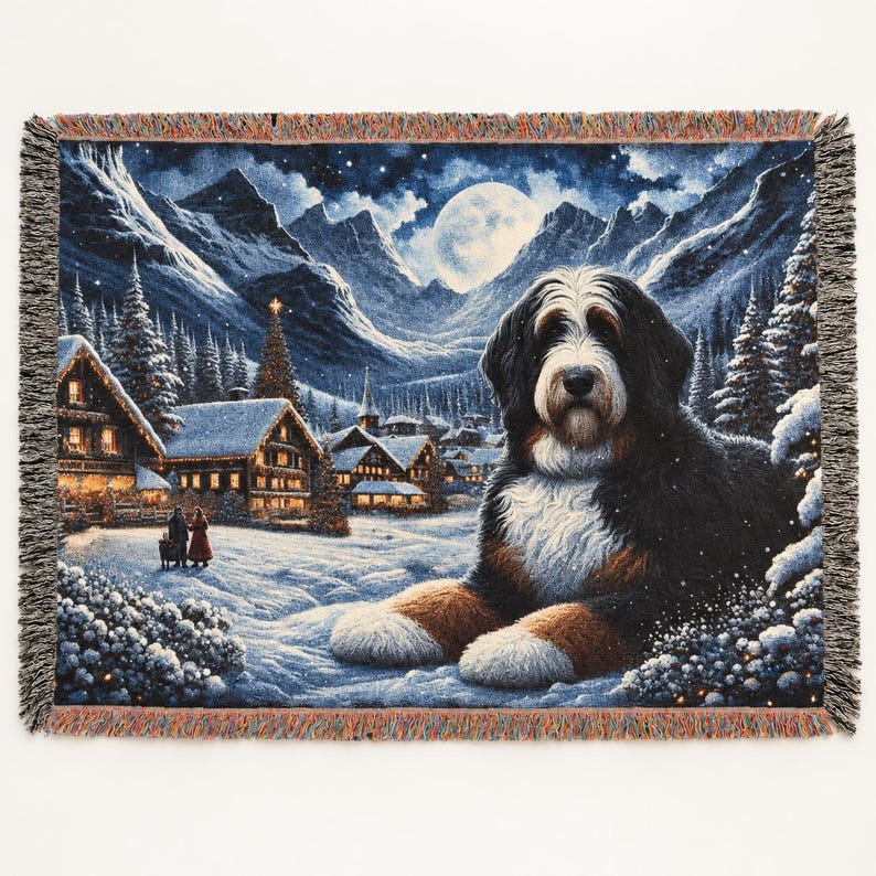 Puede incluir: Una manta tejida que muestra a un perro de monta&ntilde;a de Berna descansando frente a un pueblo invernal nevado de noche, con casas iluminadas, monta&ntilde;as cubiertas de nieve, una luna llena y bordes con flecos.