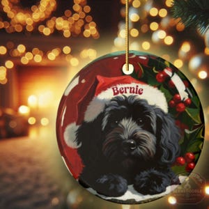 A black bernedoodle dog wearing a santa hat that is personalized with their name on it in this adorable Ceramic ornament!  Design appears on the front and the back of this doodle dog ornament!