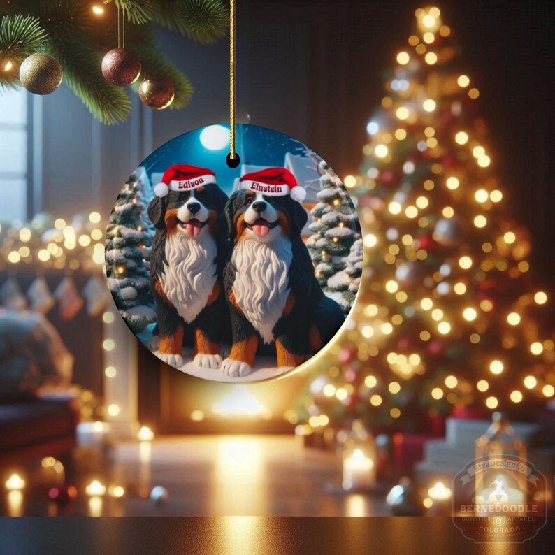 Op de afbeelding: Een ronde kerstversiering met twee Berner Sennenhonden met kerstmutsen. De honden zijn zwart, bruin en wit, met de namen "Edison" en "Einstein" op hun mutsen. De achtergrond bevat een kerstboom en besneeuwde bomen.
