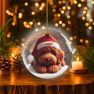 This ceramic ornament features a cute red mini-doodle golden doodle or goldendoodle dog wearing a Santa hat in a snow globe setting, surrounded by holiday decorations. Perfect for adding a festive touch to your Christmas tree or as a thoughtful gift for dog lovers.