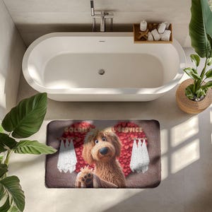 A cute golden doodle stands in front of a fluffy red heart backdrop, holding a brown towel on a cozy bath mat. White towels hang on either side, creating a spa-like feel. The text “Goldie’s Towel Service” sits above the doodle. Perfect for dog lovers, bathroom décor, and pet-themed home accents.