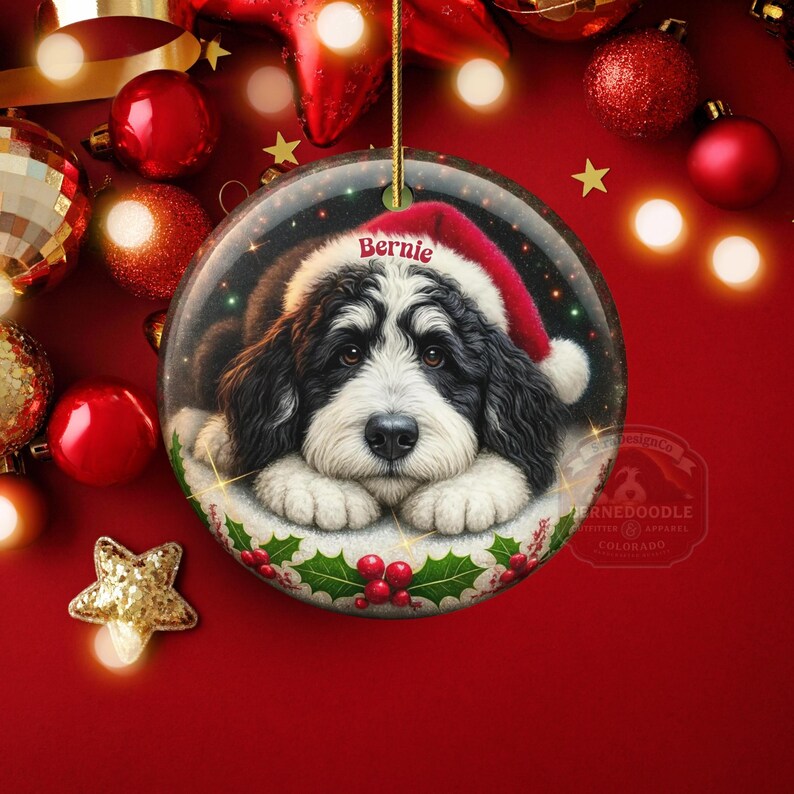 May include: A round Christmas ornament featuring a Bernedoodle dog wearing a Santa hat. The dog's name, "Bernie," is printed on the hat. The ornament is surrounded by red and gold Christmas decorations.