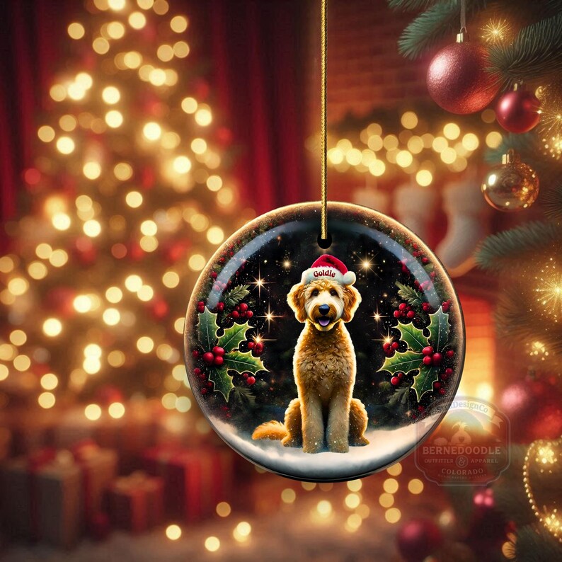 May include: A round Christmas ornament featuring a Goldendoodle wearing a Santa hat. The ornament has a black background with stars, holly, and berries. The ornament is hanging from a gold string.
