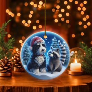 A 3-inch double-sided ceramic Christmas ornament featuring an adorable claymation-style Bernedoodle wearing a red Santa hat personalized  sitting beside a cute raccoon under a snowy winter night sky. The ornament has crisp detailing, soft blue tones, and a warm Christmas glow in the blurred background. Perfect for Bernedoodle lovers, handmade Christmas gift shoppers. High-quality ceramic with vibrant colors, ideal for tree decorating, pet memorial ornaments, or festive seasonal displays.