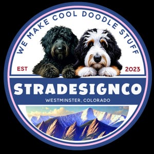 May include: A circular logo featuring a black dog and a tri-color doodle dog above the text STRADESIGNCO, WESTMINSTER, COLORADO, EST 2023, and WE MAKE COOL DOODLE STUFF. The bottom section displays a mountain range with snow-capped peaks under a blue sky.