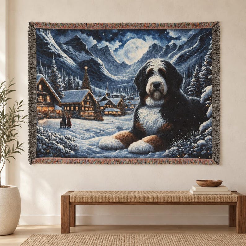 Puede incluir: Una manta de tapiz tejida que muestra a un perro de monta&ntilde;a de Berna descansando en una escena de pueblo invernal nevado por la noche. El fondo muestra monta&ntilde;as nevadas, una luna llena y casas iluminadas bajo un cielo estrellado con flecos.