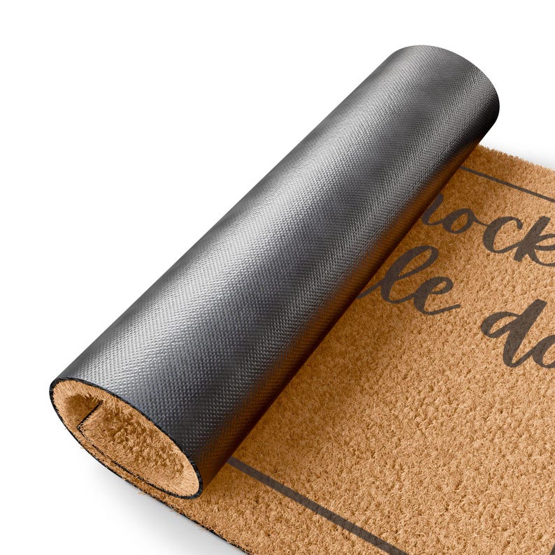 May include: A rolled-up brown doormat with black text that reads "knock le do". The mat has a dark gray, textured backing. The doormat is made of a natural fiber material.