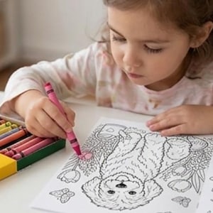 K&ouml;nnte beinhalten: Ein rosa Wachsmalstift in einer Hand, der eine schwarz-wei&szlig;e Strichzeichnung eines flauschigen Hundes umgeben von Blumen und Schmetterlingen auf einem wei&szlig;en Blatt Papier ausmalt, mit einer Schachtel bunter Wachsmalstifte auf dem Tisch.