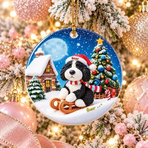 A decorative ornament featuring a black and white dog wearing a Santa hat and riding a sled, with a snowy village scene and a Christmas tree in the background.