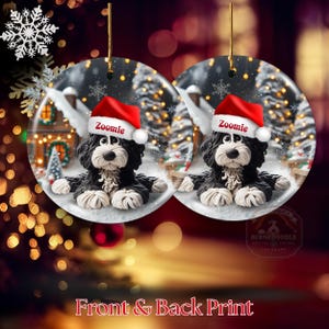 May include: Two round Christmas ornaments featuring a black and white dog wearing a red Santa hat with the name "Zoomie". The ornaments have a winter scene background with snow, trees, and a house. The text "Front & Back Print" is at the bottom.