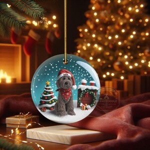 May include: A round Christmas ornament featuring a dog wearing a Santa hat and a red bandana. The ornament has a snowy scene with a Christmas tree and a chimney. The dog's name, "Latte", is on the hat.