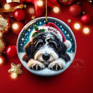 May include: A round Christmas ornament featuring a Bernedoodle dog wearing a Santa hat with the name "Bernie". The ornament has a snowy background with twinkling lights and is surrounded by red Christmas decorations.