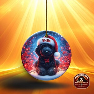 Capture the magic of the season with this adorable black Goldendoodle puppy wearing a festive Santa hat, surrounded by glowing red berries and twinkling snowflakes! Perfect personalized Christmas tree ornament for doodle parents. Add your dog's name (like "Stella") for a heartfelt touch. High-quality ceramic, vibrant print, gold string included. Ideal dog mom/dad gift, stocking stuffer, or memorial keepsake. Handmade holiday charm!