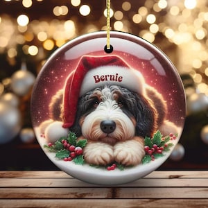Personalize your holiday decor with this charming Bernedoodle Christmas ornament! Featuring a cute Bernedoodle in a festive Santa hat and customizable name, this round ornament adds warmth and joy to any tree. Perfect for dog lovers and unique gifts!