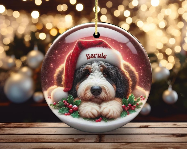 Personalize your holiday decor with this charming Bernedoodle Christmas ornament! Featuring a cute Bernedoodle in a festive Santa hat and customizable name, this round ornament adds warmth and joy to any tree. Perfect for dog lovers and unique gifts!