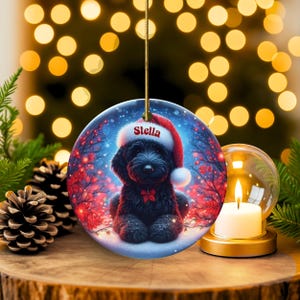 Capture the magic of the season with this adorable black Goldendoodle puppy wearing a festive Santa hat, surrounded by glowing red berries and twinkling snowflakes! Perfect personalized Christmas tree ornament for doodle parents. Add your dog's name (like "Stella") for a heartfelt touch. High-quality ceramic, vibrant print, gold string included. Ideal dog mom/dad gift, stocking stuffer, or memorial keepsake. Handmade holiday charm!