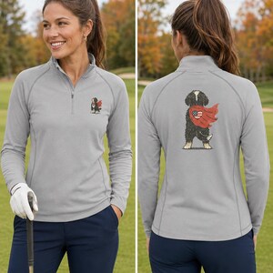 K&ouml;nnte beinhalten: Ein hellgrauer Langarm-Pullover mit kurzem Rei&szlig;verschluss, der auf der linken Brust ein kleines Motiv eines schwarz-wei&szlig;en Hundes mit rotem Umhang zeigt, sowie eine gr&ouml;&szlig;ere Version desselben Hundemotivs auf der R&uuml;ckseite zwischen den Schulterbl&auml;ttern.
