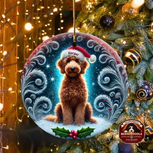 A cozy Christmas ornament featuring a goldendoodle sitting in fluffy snow while wearing a Santa hat with the name “Harper.” Frosty feather-style swirls, glittering stars, and holly berries add decorative flair. The glowing background lights create warmth and charm, making it ideal as a personalized gift or tree decoration.
