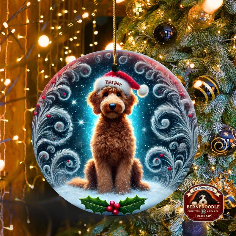 A cozy Christmas ornament featuring a goldendoodle sitting in fluffy snow while wearing a Santa hat with the name “Harper.” Frosty feather-style swirls, glittering stars, and holly berries add decorative flair. The glowing background lights create warmth and charm, making it ideal as a personalized gift or tree decoration.