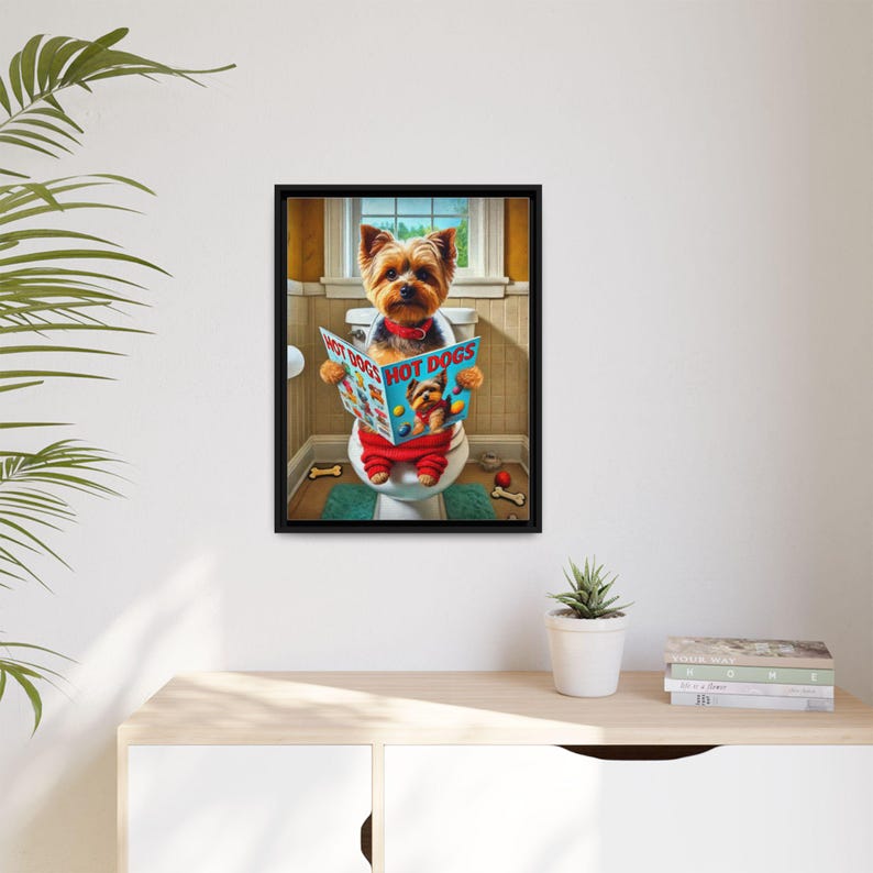 May include: A framed print featuring a Yorkshire Terrier sitting on a toilet, reading a magazine titled "HOT DOGS." The dog is wearing a red outfit and a bow tie. The bathroom setting includes a window, a green rug, and bone-shaped toys.