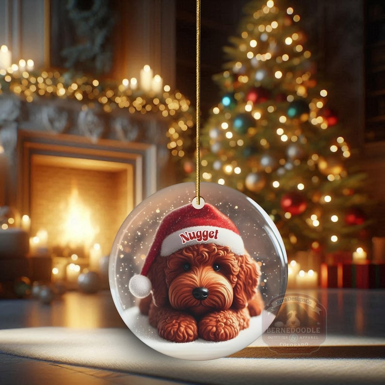 This ceramic ornament features a cute red mini-doodle golden doodle or goldendoodle dog wearing a Santa hat in a snow globe setting, surrounded by holiday decorations. Perfect for adding a festive touch to your Christmas tree or as a thoughtful gift for dog lovers.