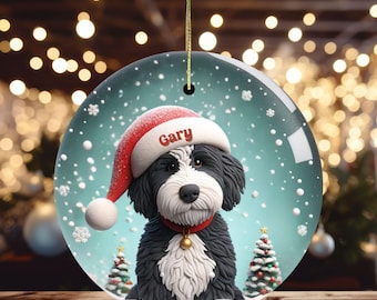 May include: A round Christmas ornament featuring a black and white dog wearing a red Santa hat with the name "Gary". The ornament has a gold string for hanging and includes two small Christmas trees and snowflakes.