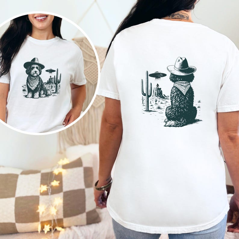 May include: White t-shirt featuring a black and white graphic of a dog wearing a cowboy hat and bandana, with a UFO and desert landscape. The design is on the front and back of the shirt.