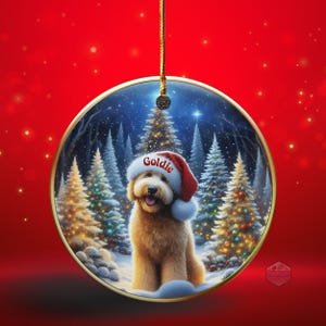 May include: A round Christmas ornament with a gold trim, featuring a fluffy, light brown dog wearing a Santa hat with the name "Goldie". The background shows a snowy forest with decorated Christmas trees.