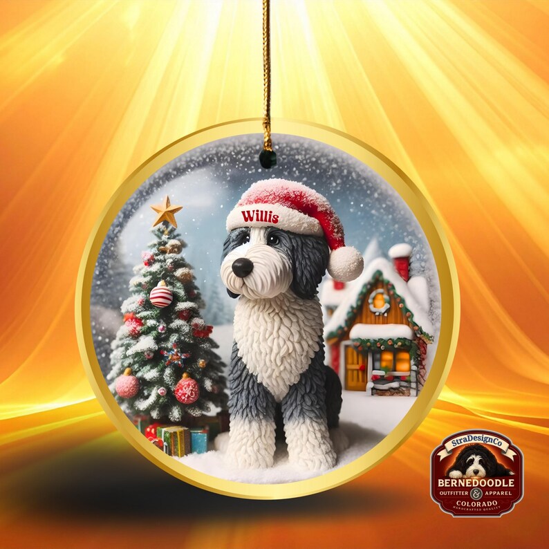 May include: A circular Christmas decoration depicting a Bernedoodle dog in a Santa hat, with the name "Willis". The ornament shows a winter scene with a Christmas tree and a snow-covered house. The decoration has a gold trim.