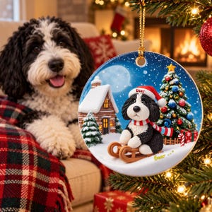 A black and white dog is sitting on a sled, wearing a Santa hat, and looking at the camera, with a Christmas tree and a fireplace in the background.