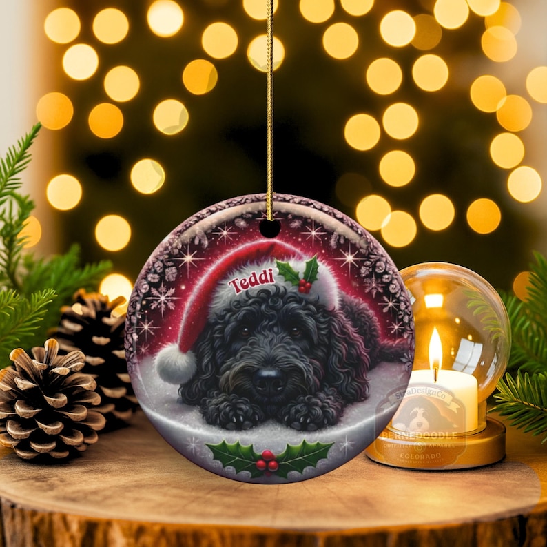 Black bernedoodle or labradoodle dog ceramic ornament show hanging with a gold string.  The ornament measures 3 inches in diameter and is a full gloss, printed on both sides.