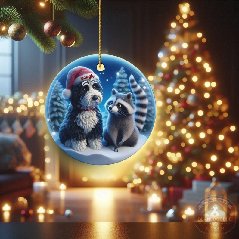 A 3-inch double-sided ceramic Christmas ornament featuring an adorable claymation-style Bernedoodle wearing a red Santa hat personalized  sitting beside a cute raccoon under a snowy winter night sky. The ornament has crisp detailing, soft blue tones, and a warm Christmas glow in the blurred background. Perfect for Bernedoodle lovers, handmade Christmas gift shoppers. High-quality ceramic with vibrant colors, ideal for tree decorating, pet memorial ornaments, or festive seasonal displays.
