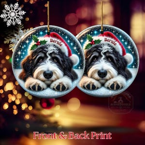 May include: Two round Christmas ornaments featuring a black and white dog wearing a Santa hat with the name "Bernie". The ornaments have a snowy background with sparkling stars and holly. The text "Front & Back Print" is at the bottom.