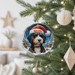 A Christmas tree decorated with ornaments, including a large ornament featuring a Bernese mountain dog wearing a Santa hat and the name " Bernie" written on it.
