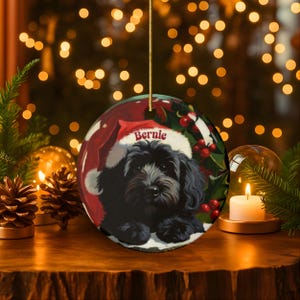 A black bernedoodle dog wearing a santa hat that is personalized with their name on it in this adorable Ceramic ornament!  Design appears on the front and the back of this doodle dog ornament!
