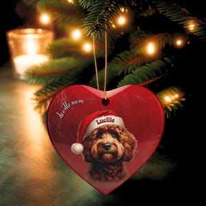 May include: Red heart-shaped Christmas ornament featuring a brown dog wearing a Santa hat with the name "Lucille". The ornament has the words "doodle mom" in script. A gold string is attached for hanging.