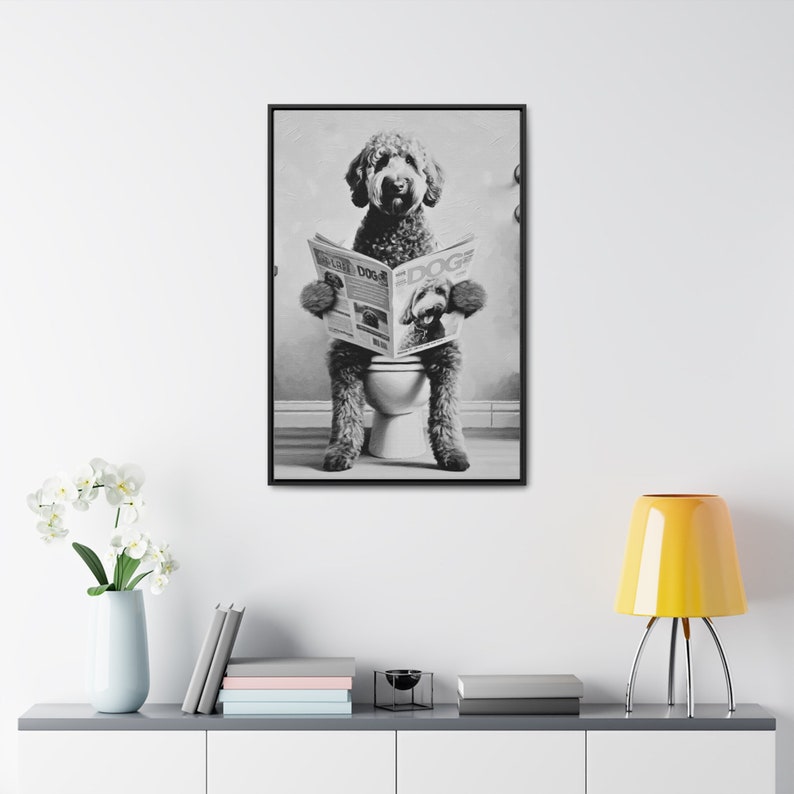May include: A black and white framed wall art print featuring a curly-haired dog sitting on a toilet while reading a newspaper titled DOG. The dog is depicted in a seated position, holding the open newspaper with both front paws in this portrait.