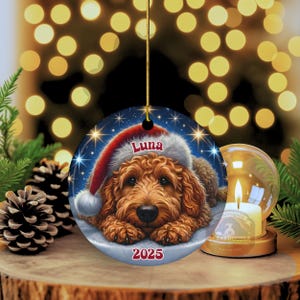 A ceramic ornament of a goldendoodle dog wearing a Santa hat, personalized with the dog's name and the year.  Gorgeously placed in a warm background with candles and Christmas lights.