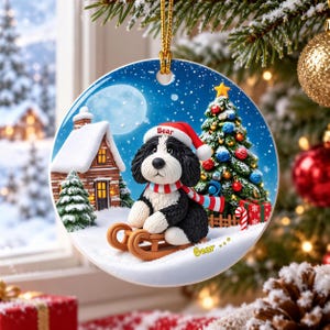 A ceramic ornament featuring a black and white dog wearing a Santa hat and scarf, sitting on a sled and looking out a window with a snowy landscape and a Christmas tree in the background.