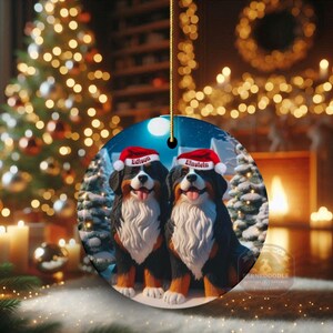 Op de afbeelding: Ronde kerstversiering met twee Bernedoodle honden met kerstmutsen met de namen "Edison" en "Einsteln". De honden staan in een besneeuwde winterlandschap met kerstbomen en een volle maan. Een gouden draad is bevestigd om op te hangen.