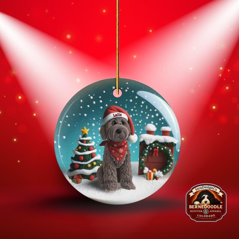 May include: A round Christmas ornament featuring a Bernedoodle dog wearing a Santa hat and bandana. The ornament has a snowy scene with a Christmas tree and a chimney. The dog's hat says "Latte".