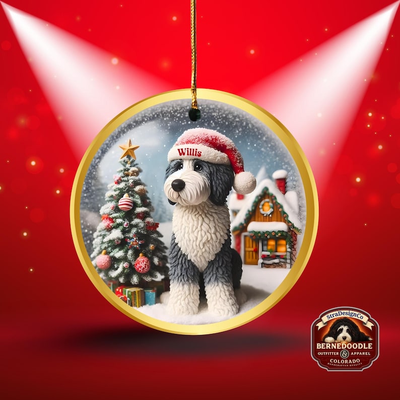 May include: A circular Christmas decoration with a gold edge, depicting a Bernedoodle dog in a Santa hat, with the name "Willis". A decorated Christmas tree and a snow-covered house are in the background. The ornament hangs from a gold string.